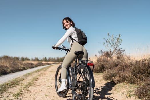 Carefree trails as a smiling woman with a backpack hops on her bike, embracing outdoor freedom and a vibrant, active lifestyle.