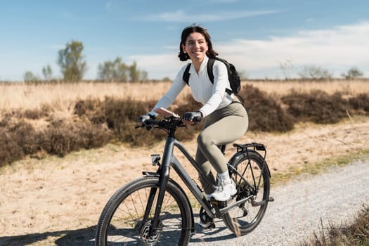 Breezy journey as a smiling woman in airy clothes pedals through a sunny day, capturing the spirit of wellness and freedom.