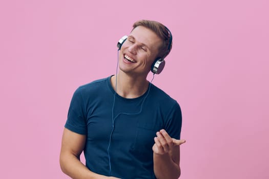 smiling young man wearing headphones and casual blue t-shirt isolated on pink background enjoying music with closed eyes and positive emotion, illustrating digital detox and mental health concept for relaxation and wellbeing