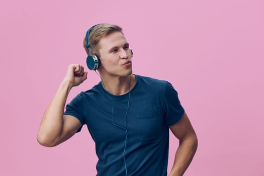 Happy young man with headphones on pink studio background, casual blue t-shirt, expressing joy and relaxation while listening to music, lifestyle, modern, youthful, vibrant atmosphere