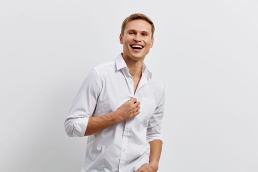 Bright portrait of a smiling man dressed in white shirt, standing in front of a plain light gray wall. He looks joyful and relaxed with a cheerful attitude, emphasizing happiness and confidence. Concept: positivity and wellness.