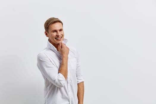 Happy young man with blonde hair wearing casual white shirt smiling confidently on plain white background studio shot, conveying friendliness and approachability. Concept: optimism and positivity
