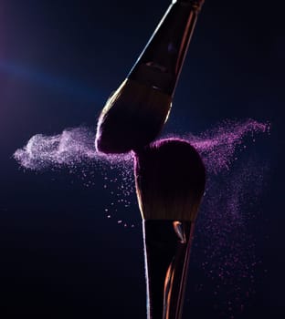 Make-up brush with pink powder explosion on black background
