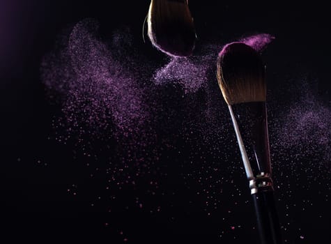 Make-up brush with pink powder explosion on black background