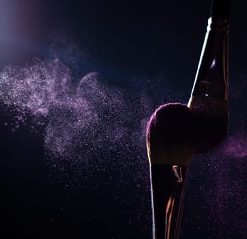 Make-up brush with pink powder explosion on black background
