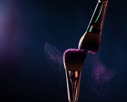 Make-up brush with pink powder explosion on black background