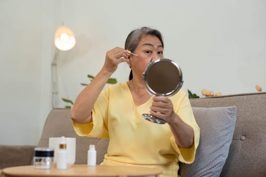 A senior woman enjoys her skincare routine, applying serum with care while admiring her reflection. This moment highlights age diversity and self-care.