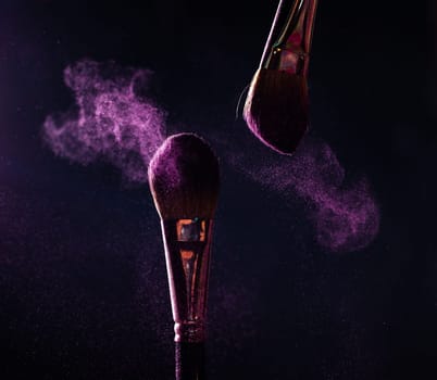 Make-up brush with pink powder explosion on black background