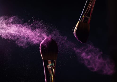 Make-up brush with pink powder explosion on black background