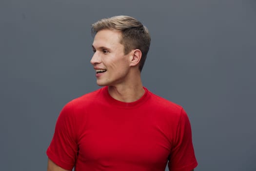 Happy young man in red t-shirt with short hairstyle smiling and looking to the side, isolated on plain gray background. Studio portrait capturing joy, confidence, casual style, positive mood and fashion concept. Concept: happiness.