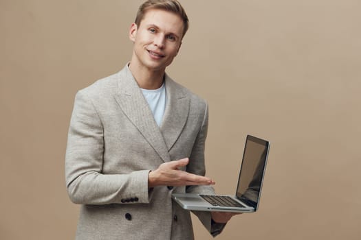 Friendly smiling man presenting laptop computer, wearing casual blazer and t-shirt, standing against plain light beige background, engaging in tech or work-related activity, concept: modern business communication.