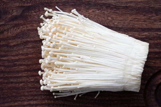 Cluster of enoki mushrooms on dark wood.