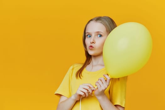 Playful girl holding a yellow balloon against a vibrant yellow backdrop, showcasing feelings of joy and celebration, ideal for special occasions and cheerful events