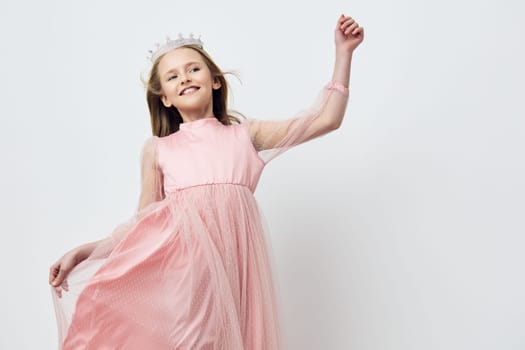 A joyful girl wearing a pink dress and a crown, twirls playfully against a soft light background, capturing the essence of childhood happiness and innocence