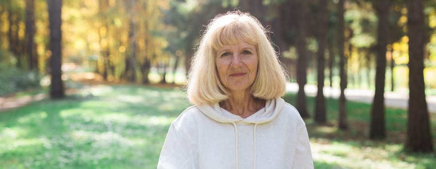 Banner mature woman enjoying a sunny walk in autumn forest, copy space. Mindfulness, relaxation and healthy outdoor lifestyle for seniors.