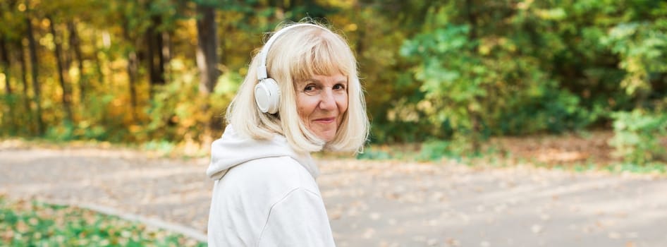 Banner senior woman walking with headphones in the park during fall, copy space. Active lifestyle, happiness, movement, freedom, and mindful aging in nature