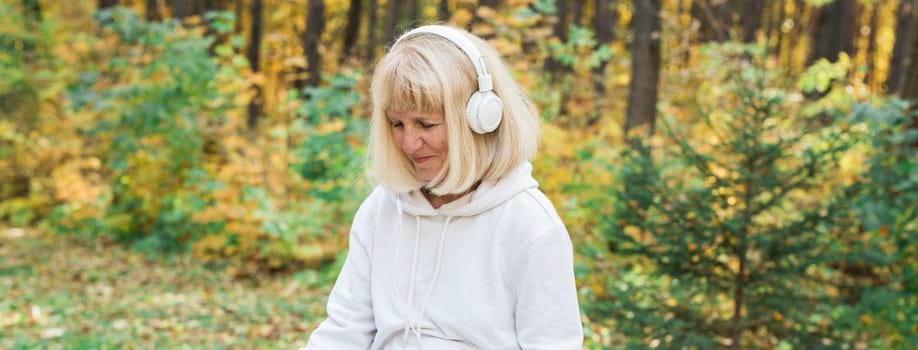 A senior woman enjoying music in the autumn forest. Relaxation, happiness, mindfulness and connection with nature during active aging.