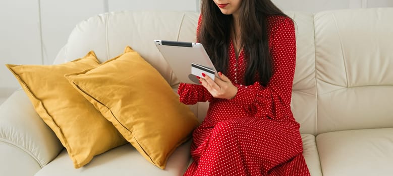 Woman shops online from home using a tablet and credit card. Concept of e-commerce and digital lifestyle comfort.