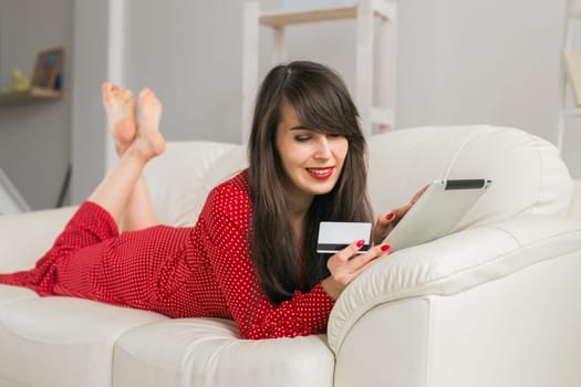 Woman uses credit card and tablet to shop online from home sofa. Digital commerce, consumer ease and modern shopping.
