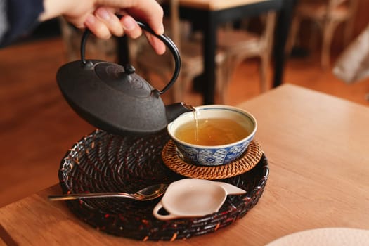 Hand pours green tea from a cast iron teapot into a cap