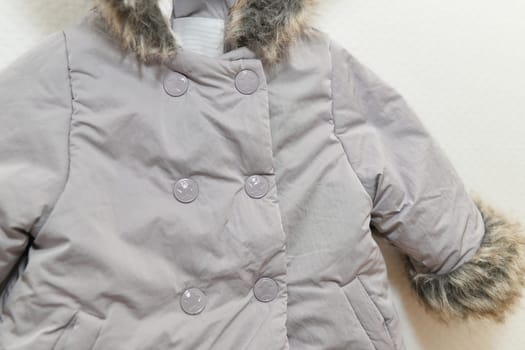 Grey-lilac colored fur jacket for girl hanging on hanger on white background