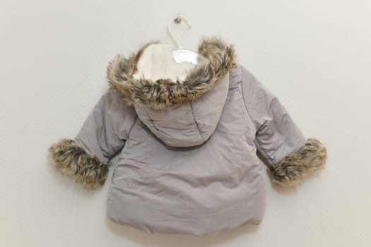 Grey-lilac colored fur jacket for girl hanging on hanger on white background