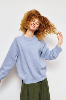 Cheerful female model with curly hair in a light blue sweater enjoys a spontaneous moment, radiating positivity and confidence The minimalist white background enhances her joyful vibe and trendy out