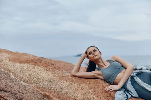 Serene young woman in stylish activewear reclining on rocky beach, embodying relaxation and fitness Ideal for health, wellness, and lifestyle projects