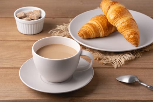Freshly baked croissants served with a hot cup of coffee on a wooden table in a cozy setting.