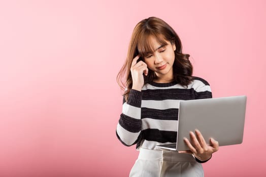 Portrait of happy Asian beautiful young woman confident smiling face holding using laptop computer looking to camera, studio shot isolated on pink background with copy space, notebook computer