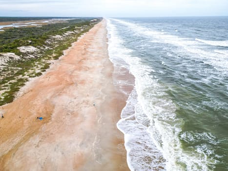 The beach features soft, golden sand that meets clear turquoise waters. Gentle waves lap at the shore, creating a tranquil atmosphere perfect for relaxation and enjoyment.