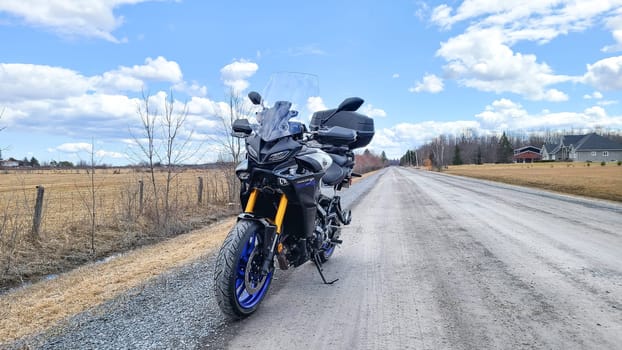 Ottawa, ON Canada - 2024-07-20: Yamaha Tracer 900 GT Motorcycle Parked on Scenic Rural Road Under Blue Sky.