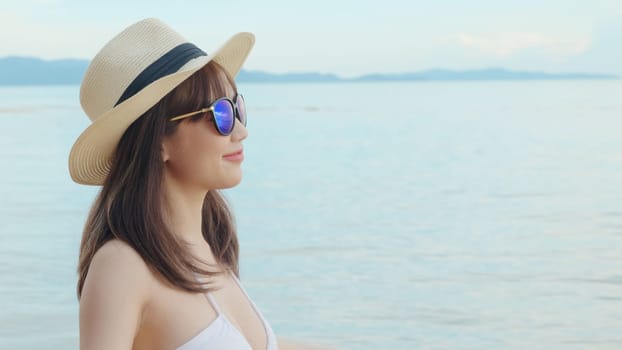Beautiful Asian woman wearing hat and sunglasses at tropical paradise beach and smiling, Happy female in bikini swimsuit having fun eyewear in holidays summer vacation travel