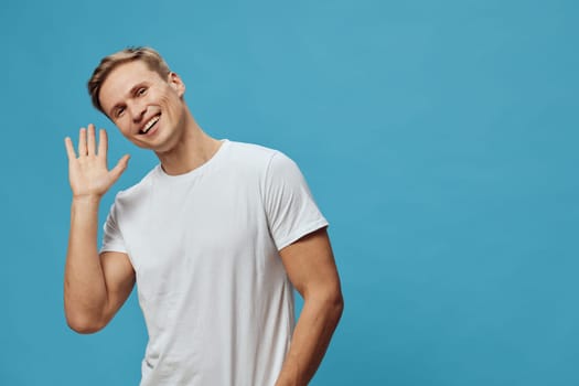 smiling caucasian man wave hand wear white t-shirt on blue background show friendly gesture happy casual look positive emotion digital detox and mental health concept