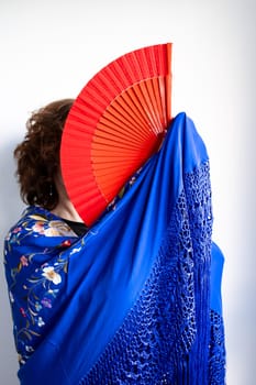 Female hidden behind red fan with blue shawl embroidery details.