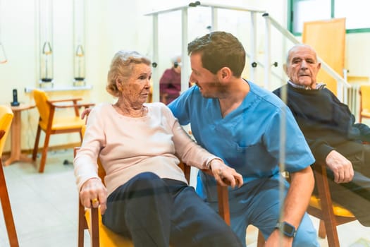 Male nurse comforting elderly woman sitting on chair in retirement home, providing care and support