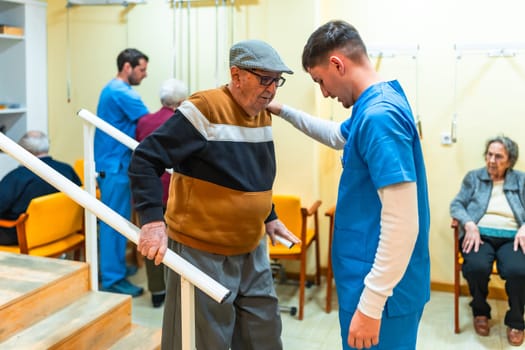 Young male nurse assisting elderly man while climbing stairs in a nursing home, providing support and care