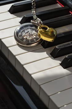 London, UK - Apr 19, 2025 - Antique pocket watch (A retro pocket watch) with Golden heart shaped love padlock on Piano keys background. The concept of the time of love, use it as your Wallpaper, Poster and Space for text, Selective focus.
