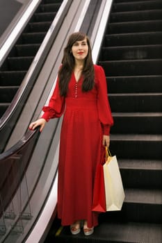 Happy woman with shopping bags on escalator. Shopping mall lifestyle and sales concept