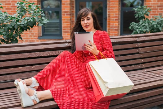 Woman sitting on bench with shopping bags and tablet. Digital lifestyle and modern shopping experience