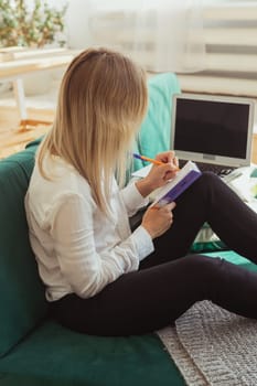 Woman writing in notebook while working remotely at home. Freelance and home office productivity theme.