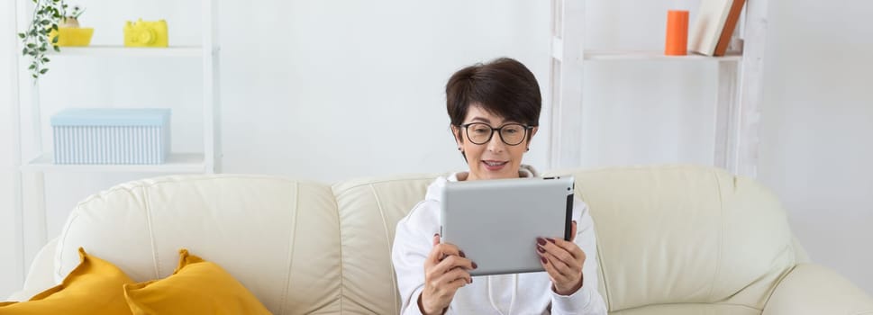 Woman using tablet while sitting on cozy couch at home. Technology and digital lifestyle concept. Banner with copy space.