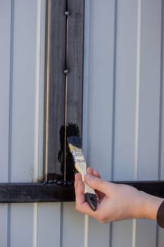 close-up of a man painting metal black with a brush.painting