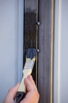 close-up of a man painting metal black with a brush.painting