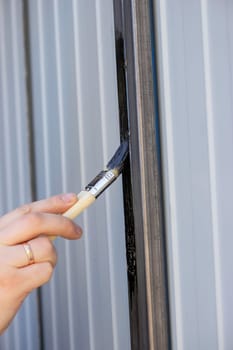 close-up of a man painting metal black with a brush.painting