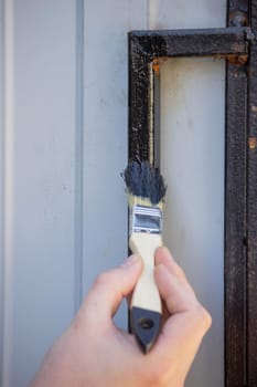 close-up of a man painting metal black with a brush.painting