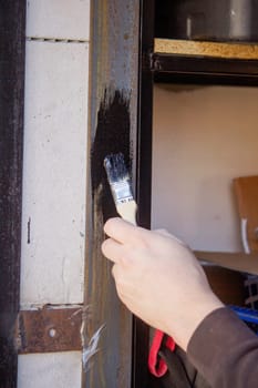 close-up of a man painting metal black with a brush.painting