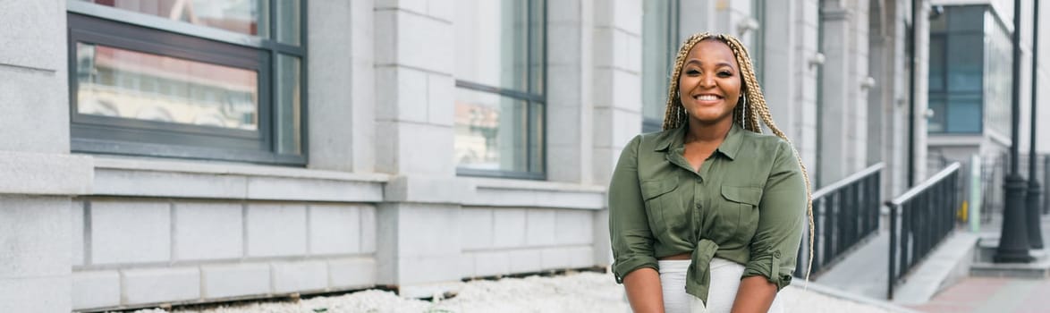 Confident african american woman standing against city architecture smiling. Concept of positivity, urban lifestyle and self-confidence.