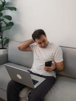 Casual man multitasking with smartphone and laptop showing thoughtful expression. Highlights themes of digital communication, decision making, adapting to modern technology challenges, problem solving