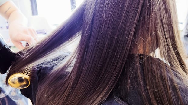 Gentle hands maneuver a hair dryer through a young girl's newly cut hair, showcasing the drying process after a meticulous trim. The warmth of the dryer breathes life into her locks, as they transform from damp to styled with care and expertise.